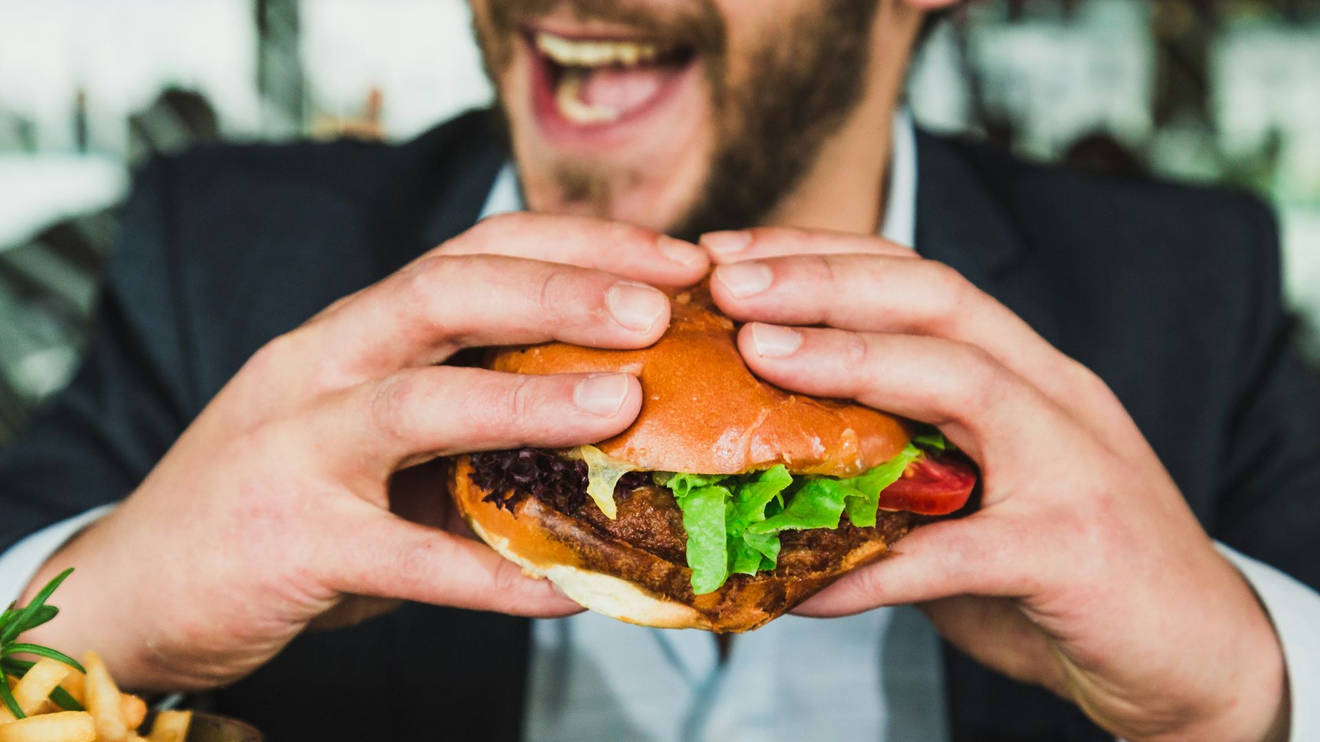 person holding burger bun with vegetables and meat