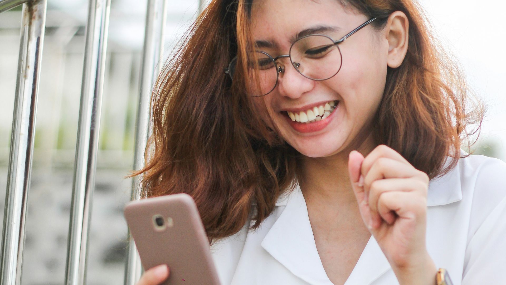 A woman in a white shirt laughing while looking at her smartphone
