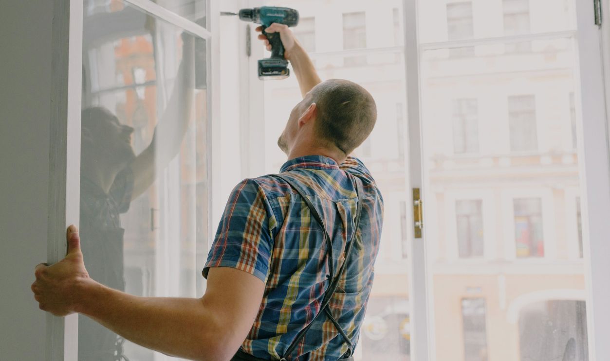 Man installing window indoors with a drill