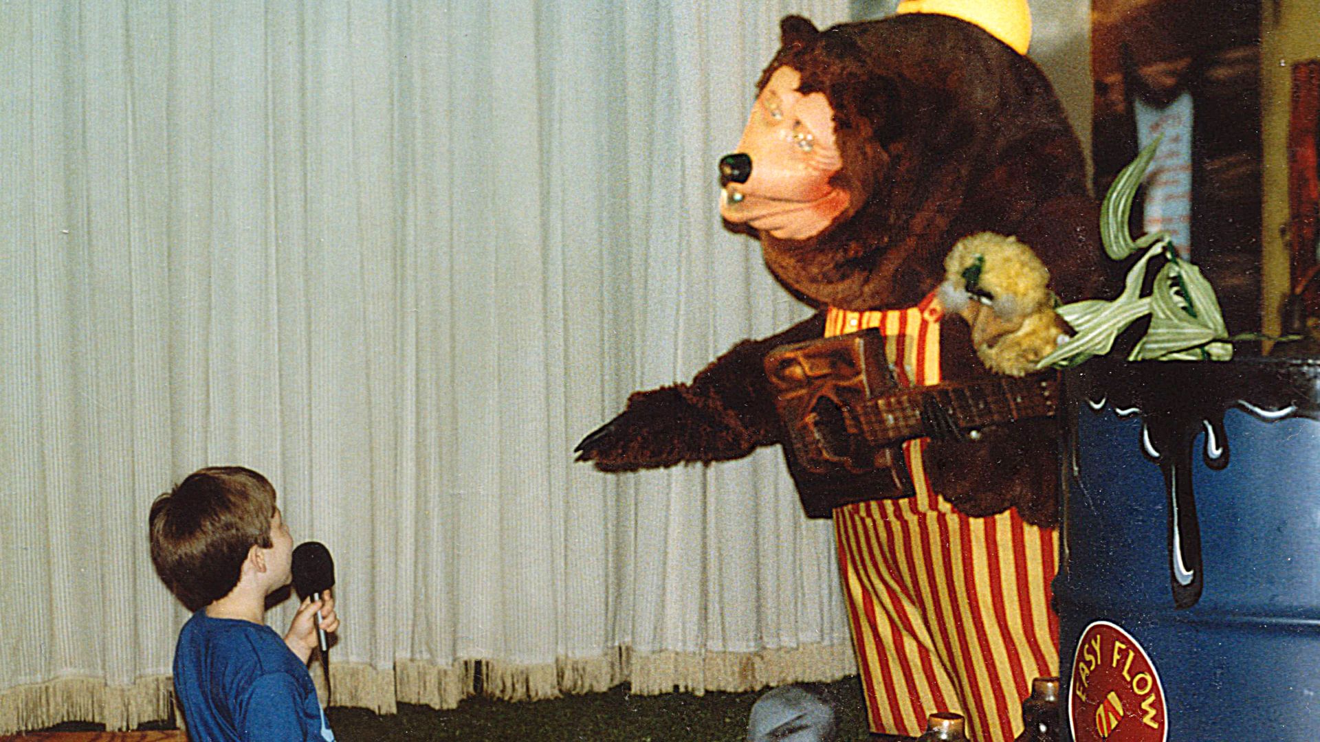 A child uses a microphone to speak to Billy Bob, mascot of ShowBiz Pizza Place, during a birthday party at ShowBiz Pizza in Fayetteville, Arkansas.  The child is Ben Schumin, i.e. User:SchuminWeb.
