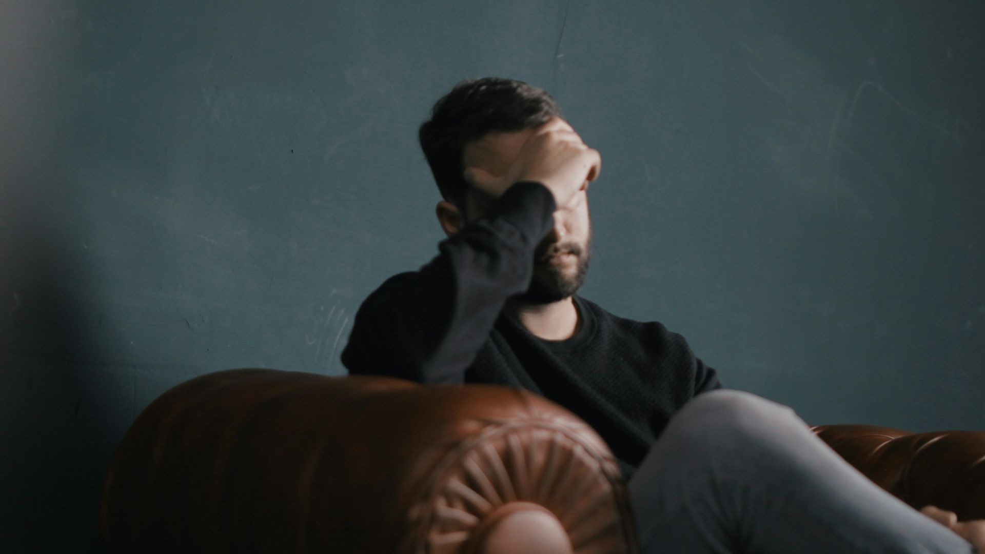 a man holds his head while sitting on a sofa