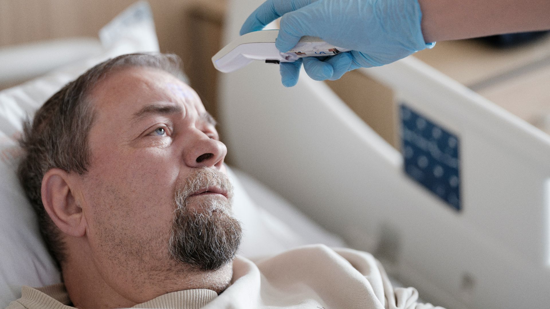 a man laying in a hospital bed with a thermometer in his hand