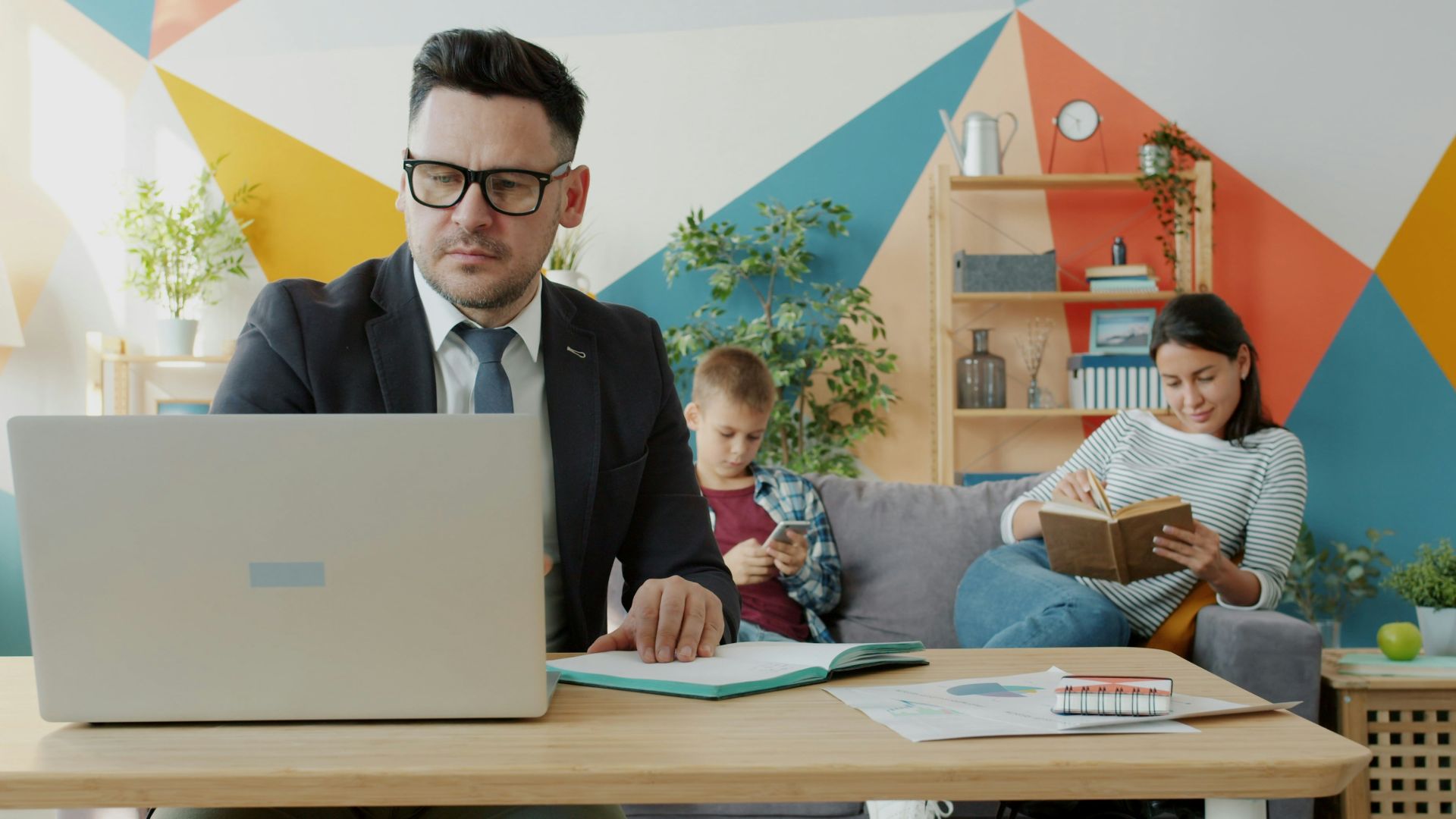 Man working on laptop while family relaxes in background