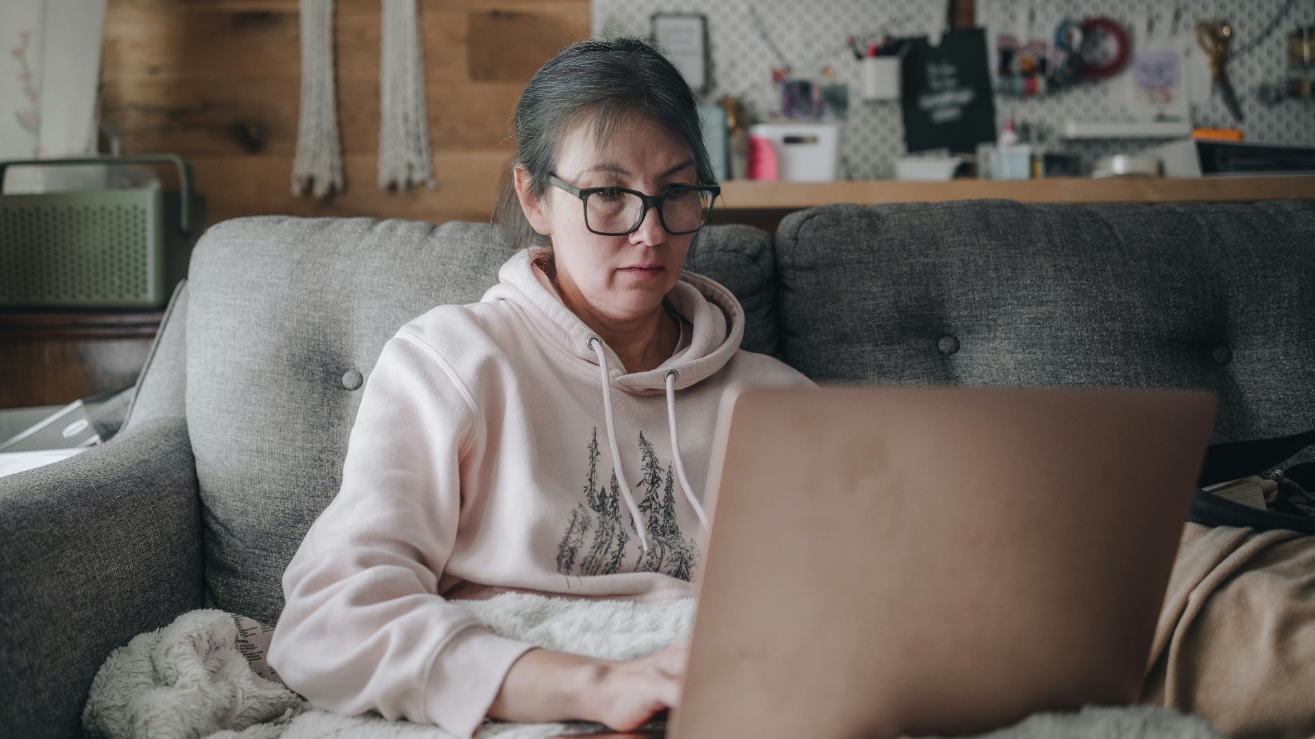 Woman works on laptop while sitting on a couch.
