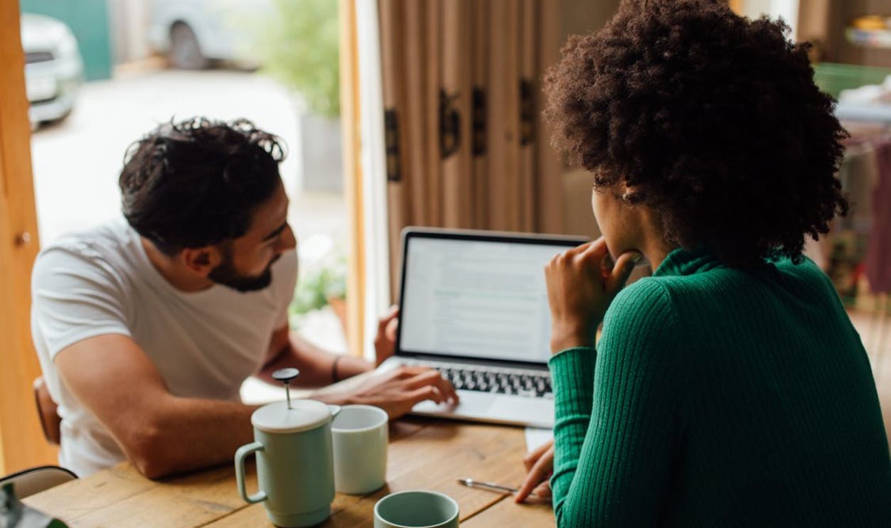 Man and Woman Sitting at Table Using Macbook