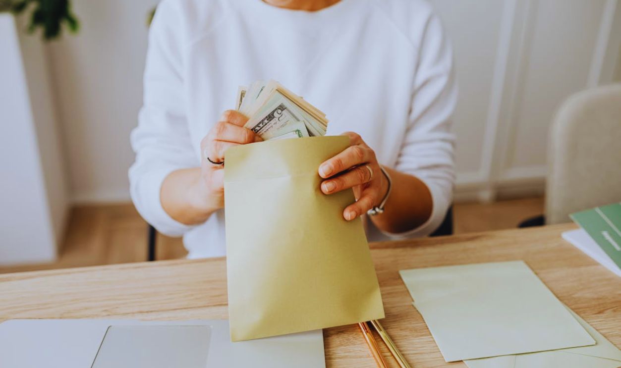 Person Wearing a Sweater Putting Money Inside an Envelope