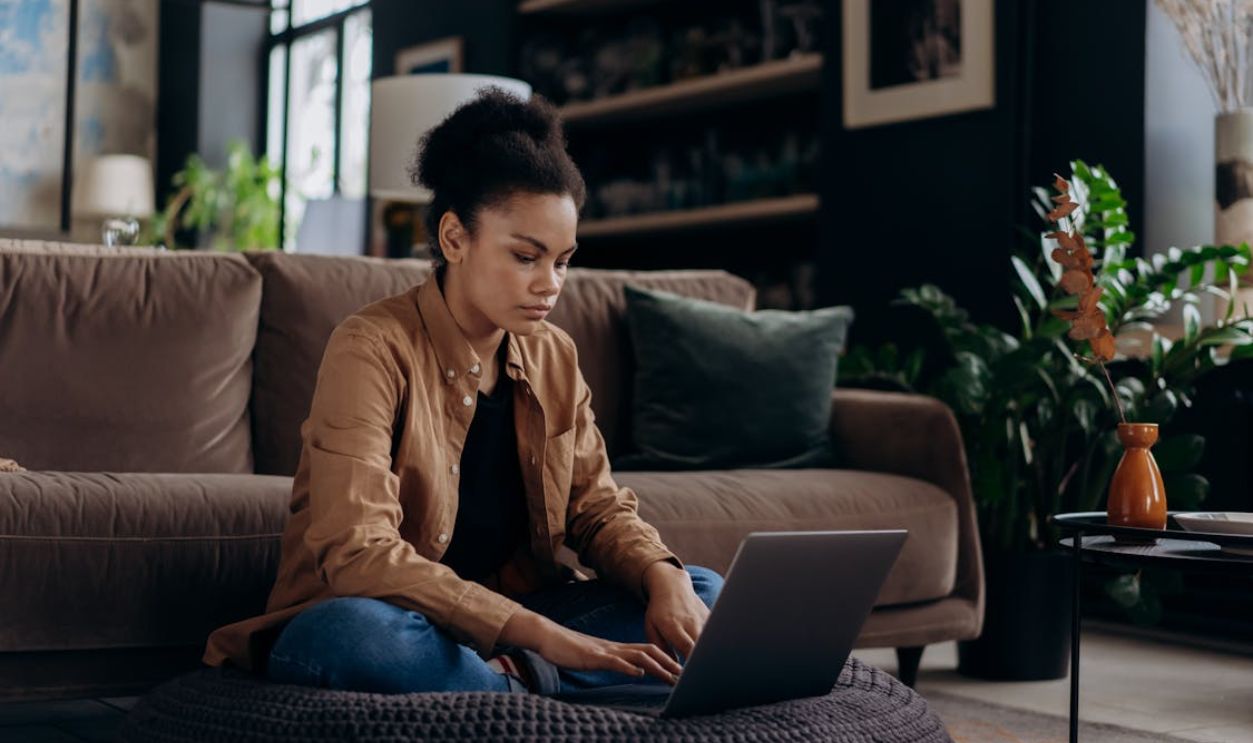 Woman Sitting on Black Knitted Floor Cushion while Using Laptop