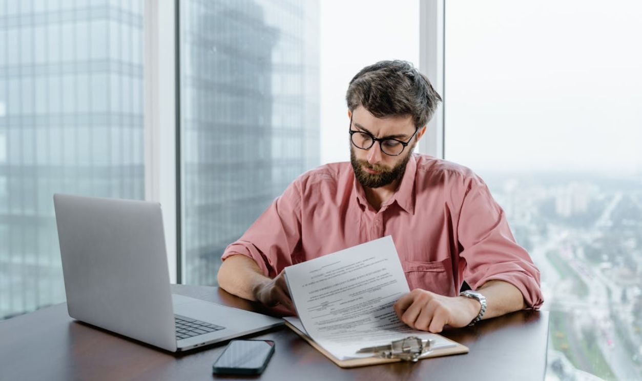 A Man in Pink Long Sleeves Wearing Eyeglasses while Looking at the Papers on the Table
