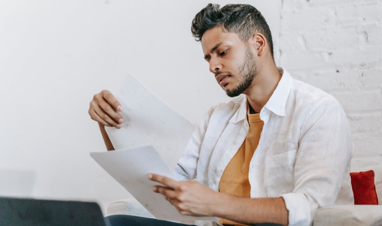 Attentive ethnic man reading documents on armchair