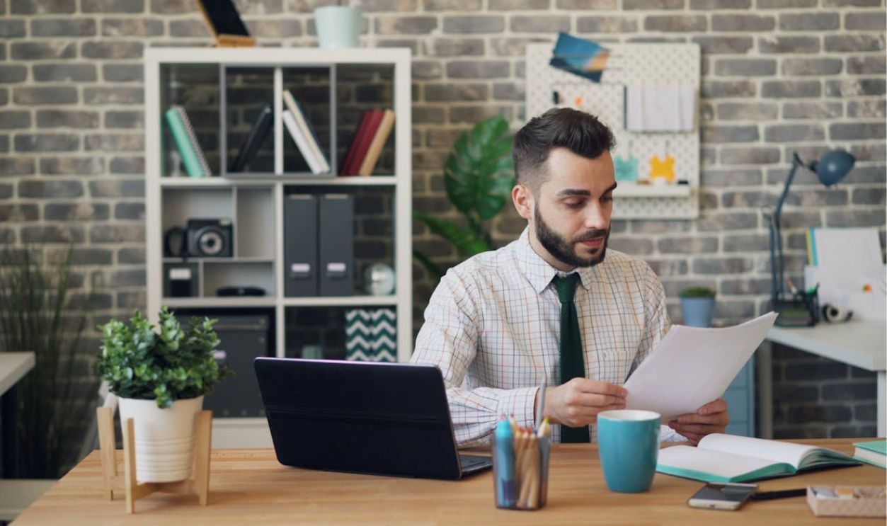 Man in Shirt Sitting at Office and Reading Document