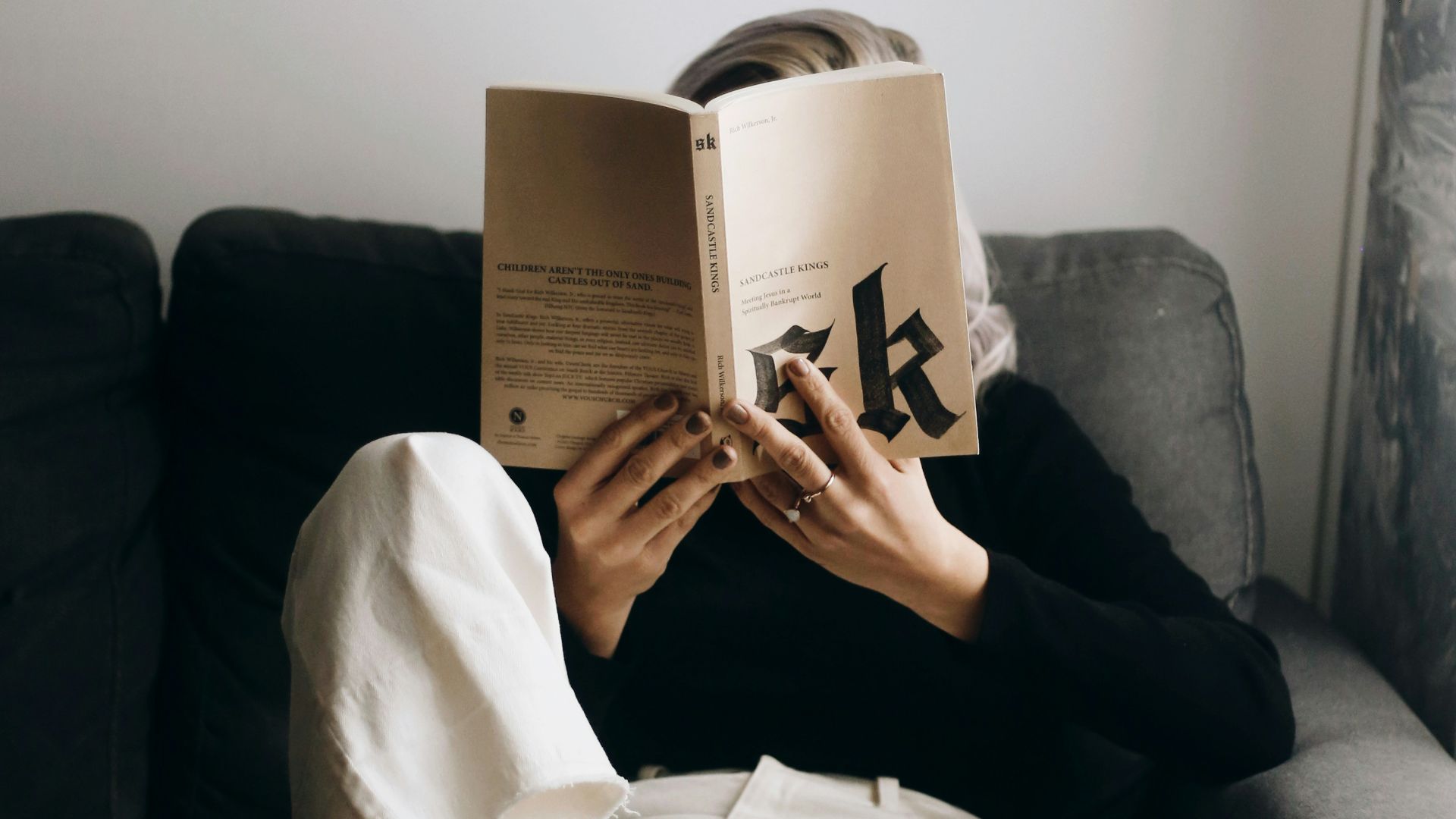 woman in white shirt reading book sitting on black sofa