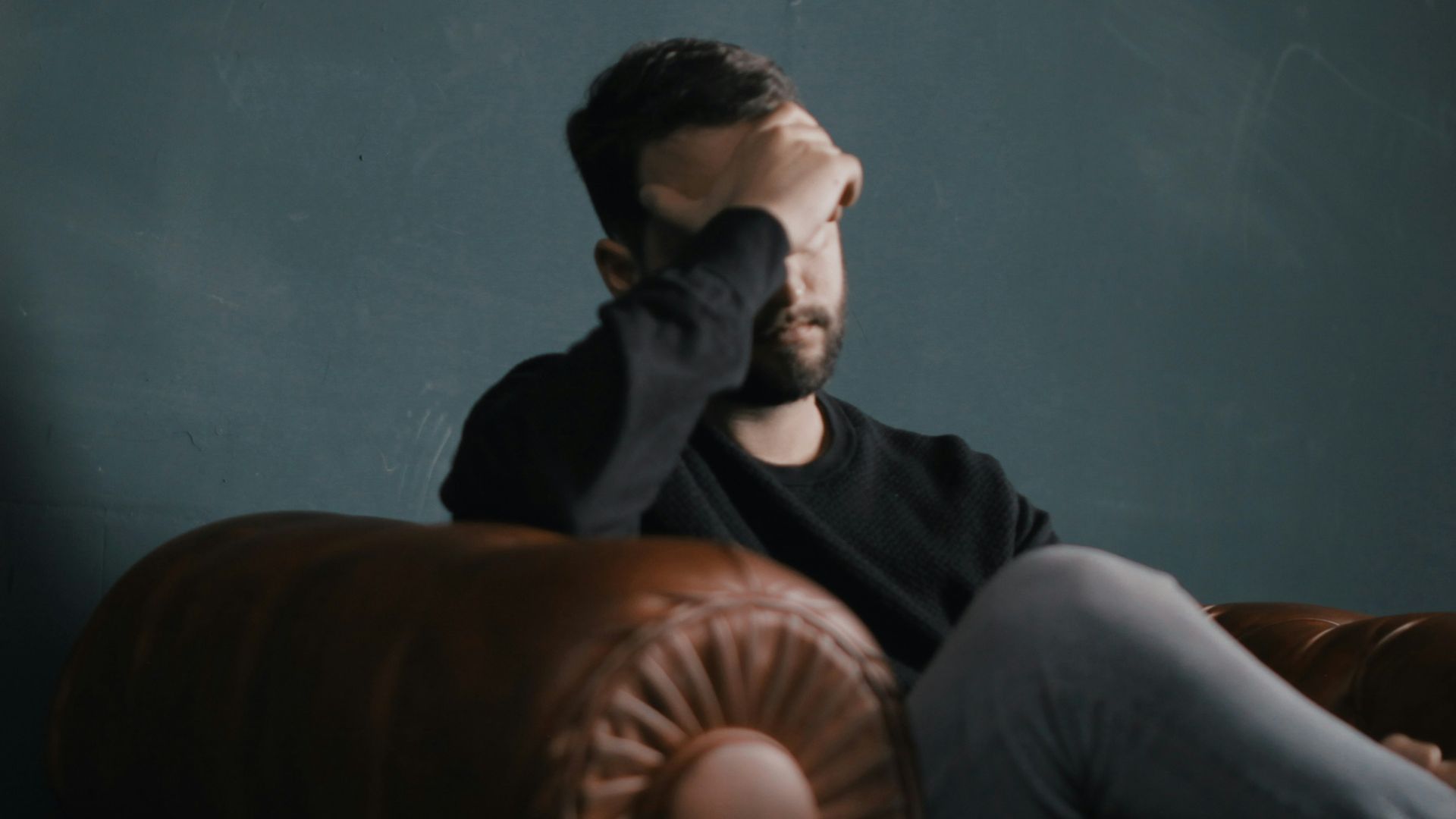 a man holds his head while sitting on a sofa