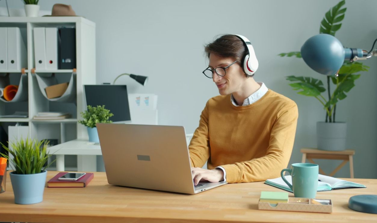 guy wearing wireless headphones is listening to music in modern office at work at table