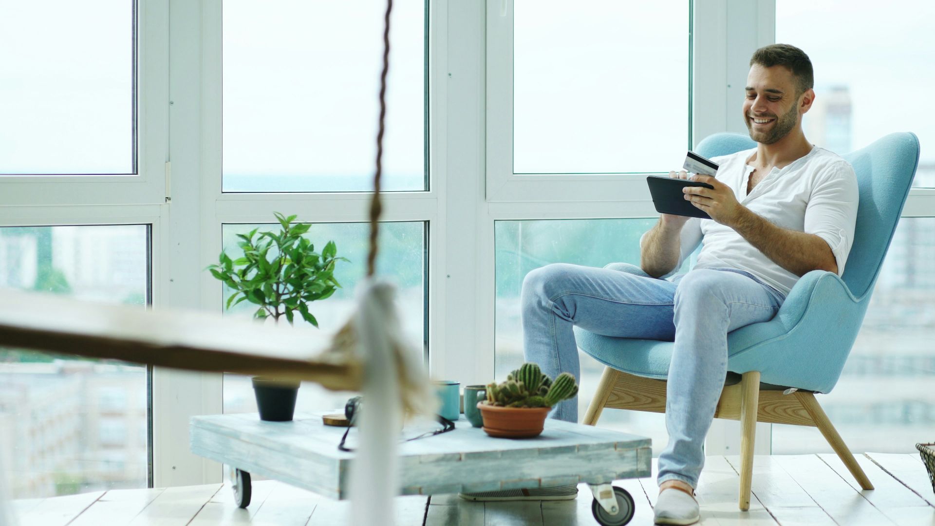 Man sitting in armchair using tablet and credit card.