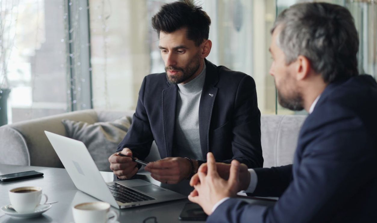 Two men in business attire sitting at a table with laptops