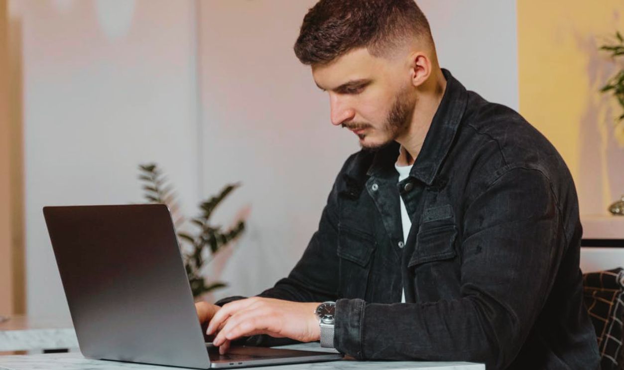Man in Black Denim Jacket Using Laptop