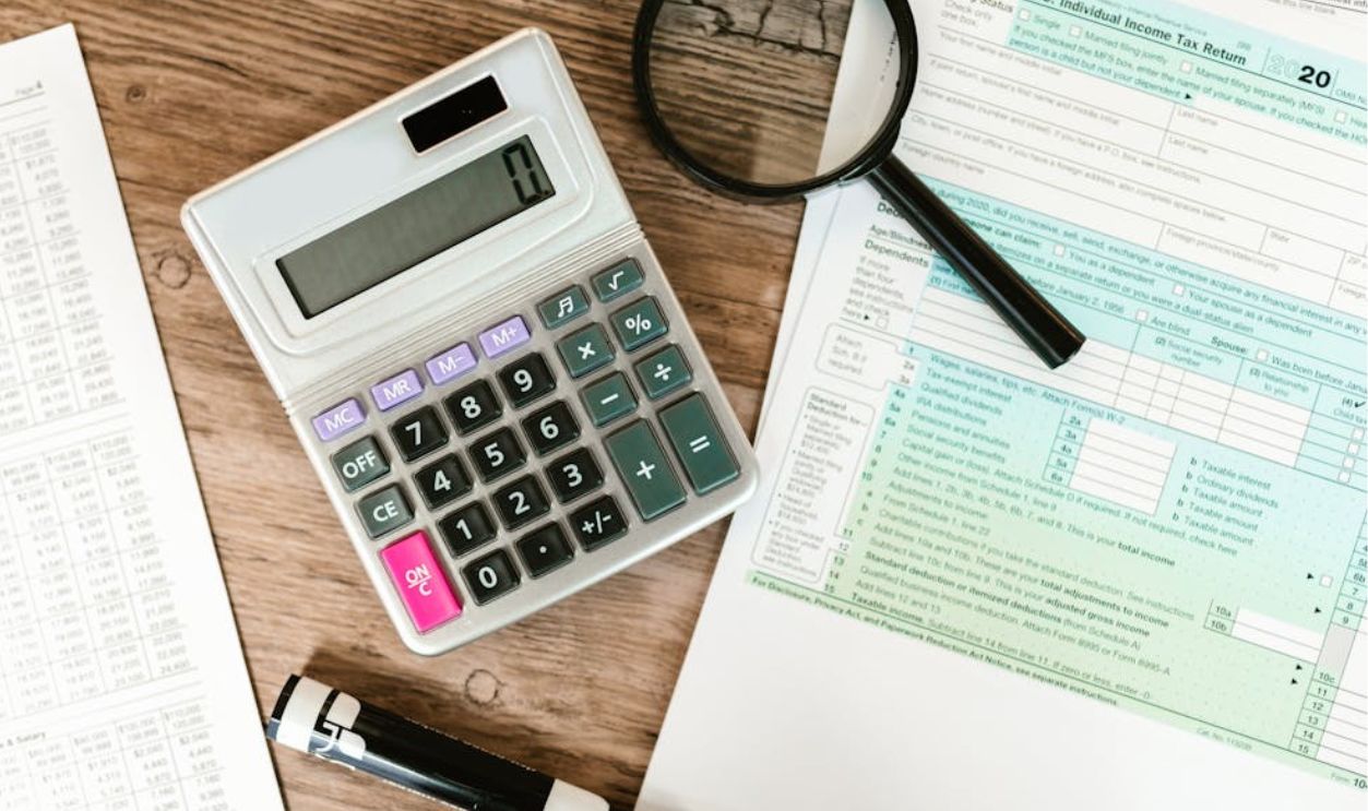 Gray Calculator and Black Magnifying Glass on Brown Wooden Surface