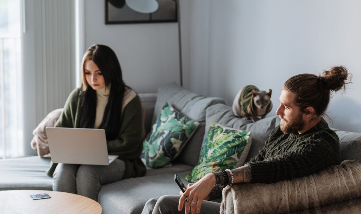Man with smartphone near girlfriend with laptop and cat indoors
