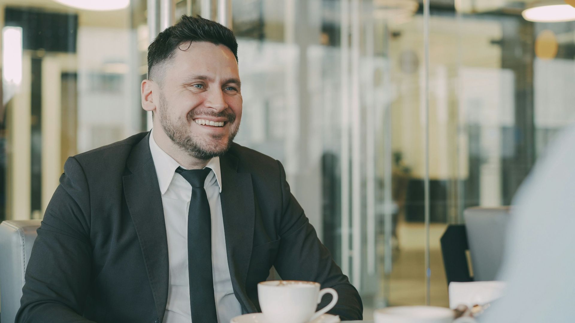 Man in suit smiling at cafe table with coffee