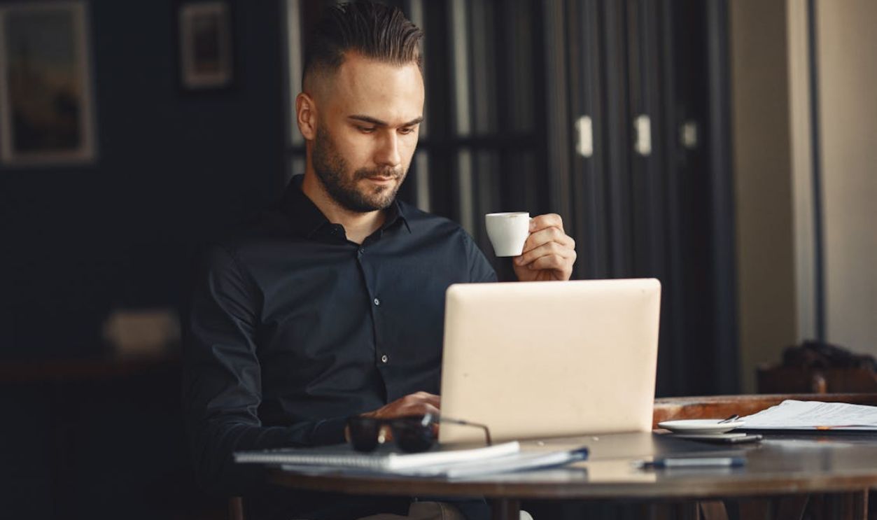 Man with Coffee Cup Working on Laptop