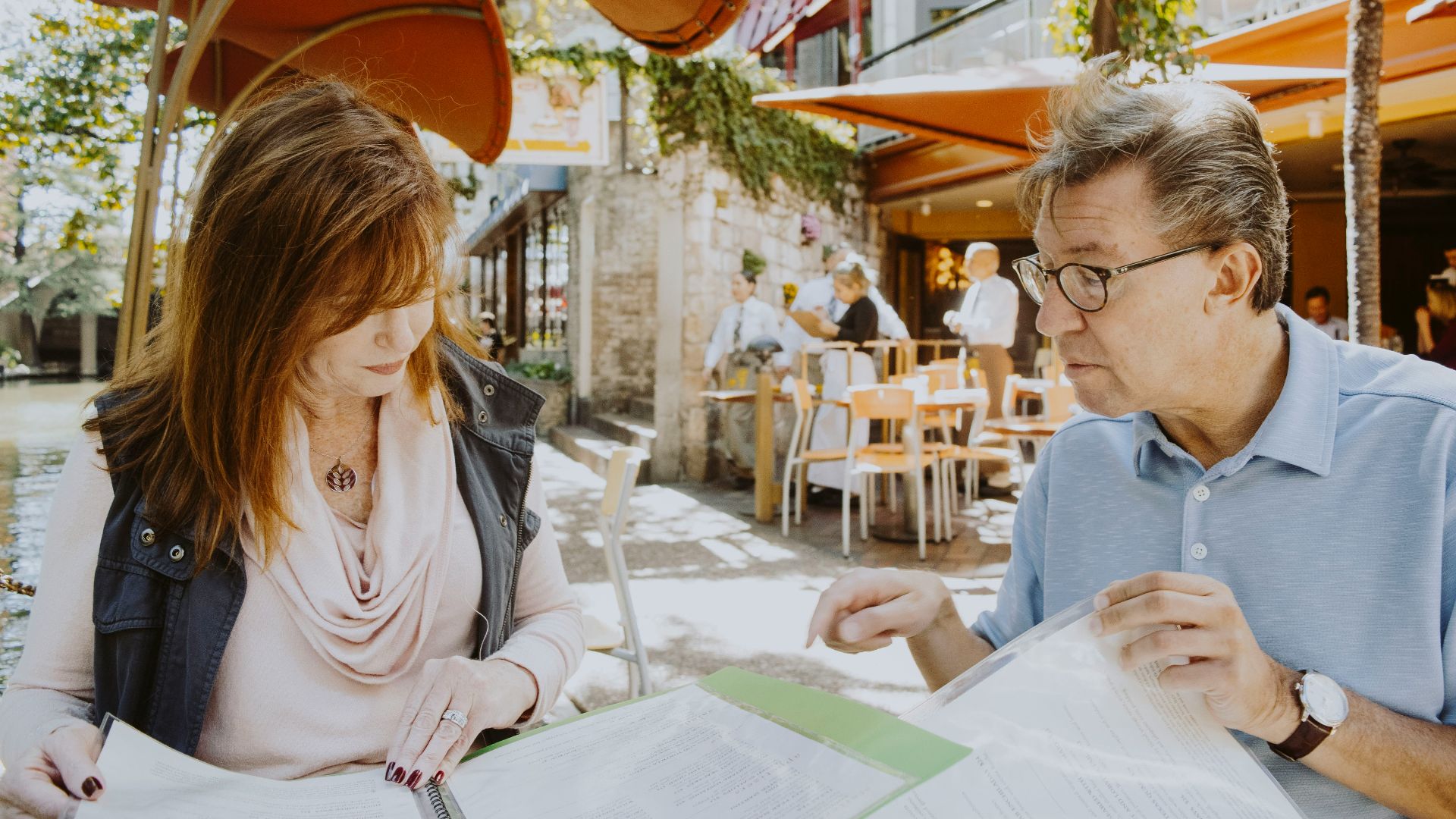 man and woman sitting down near table while reading outside cafe during daytime