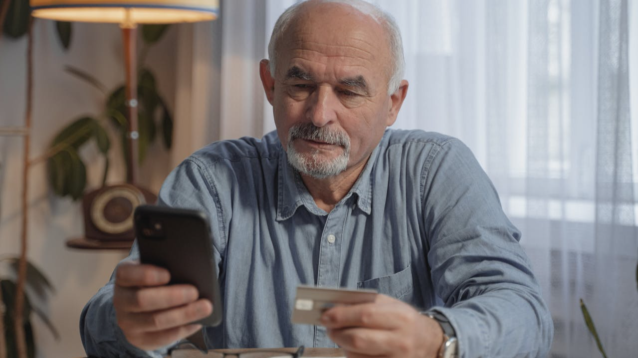 An Elderly Man Holding His Mobile Phone and a Credit Card