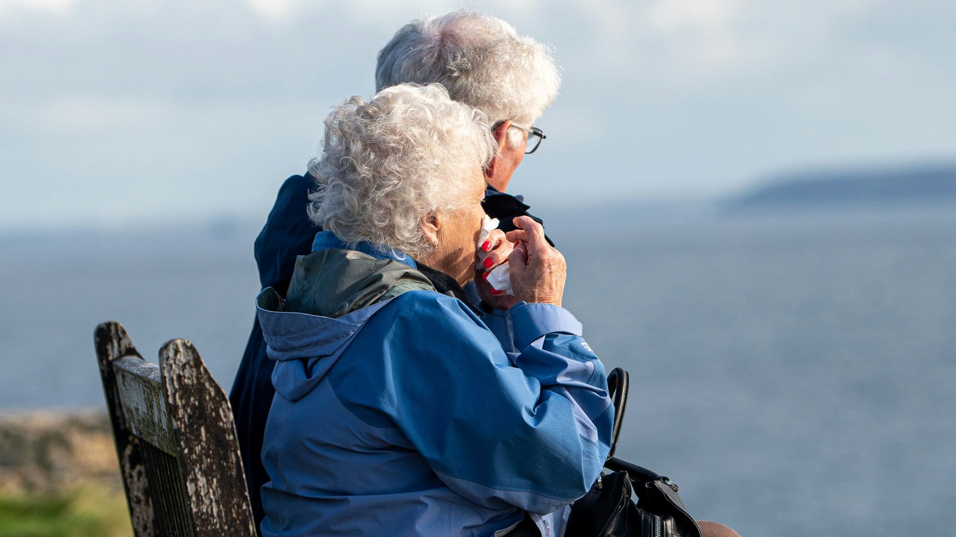 man and woman sitting on gray wooden bench viewing blue sea during daytime
