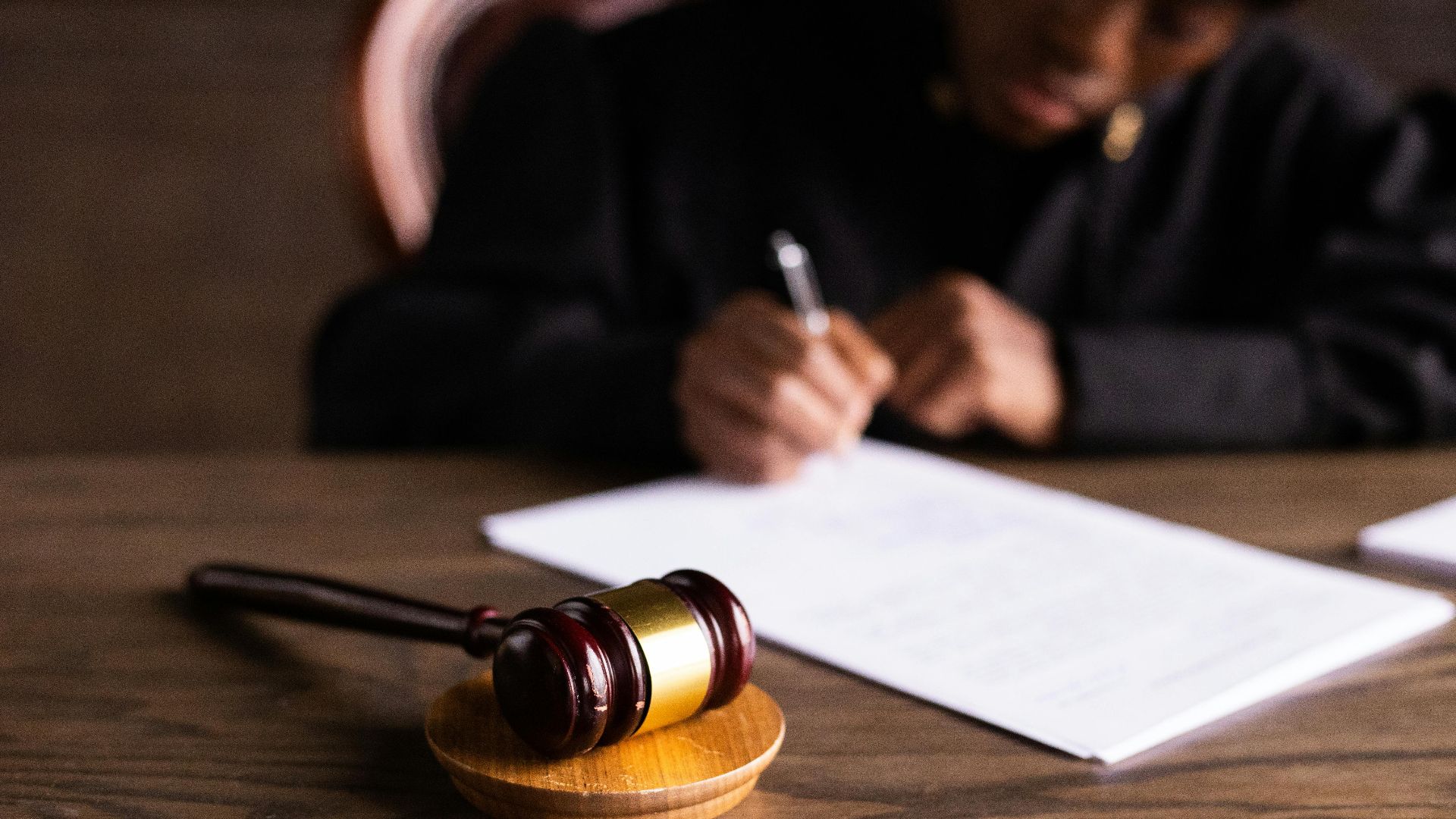 Judge signing documents at desk with focus on gavel, representing law and justice.