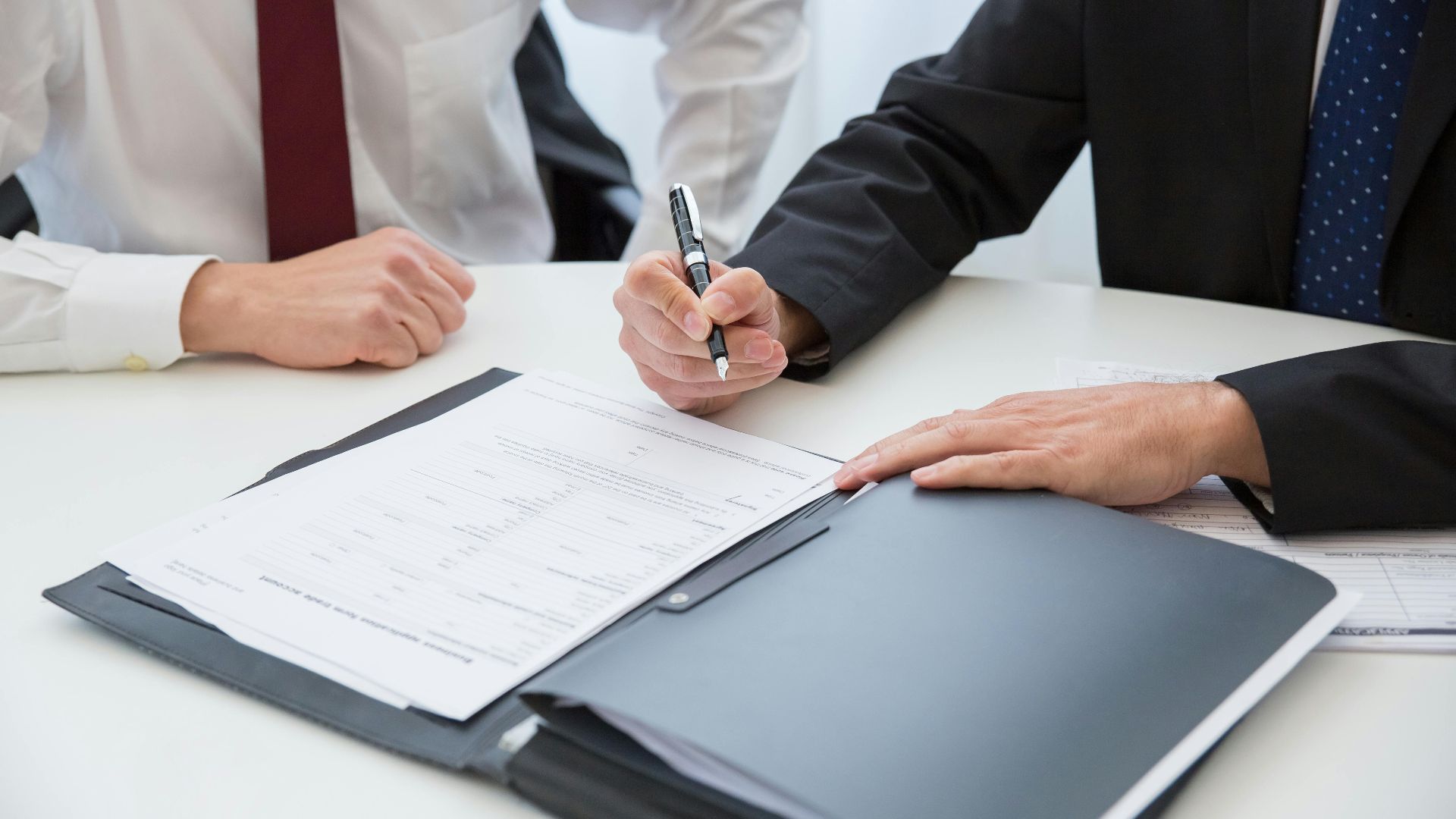 Two professionals signing a contract at a business meeting in an office.