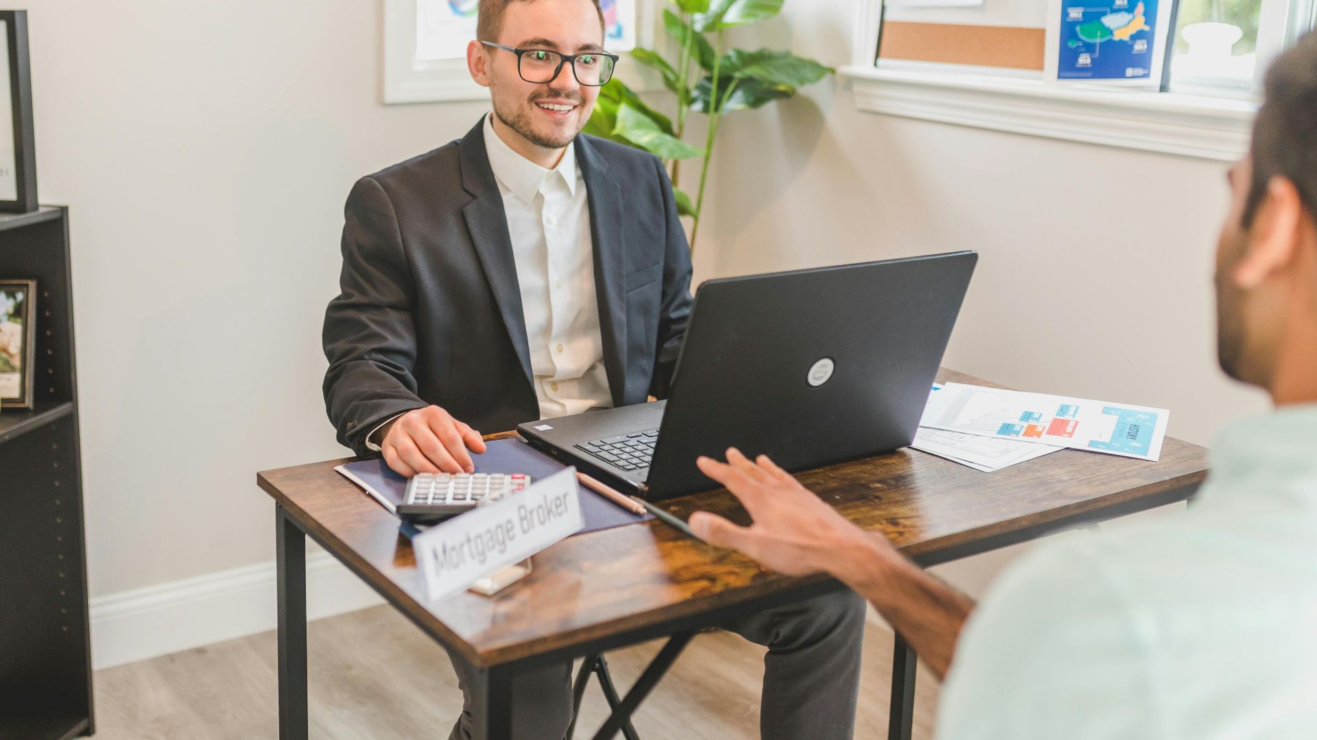 Mortgage broker in an office meeting with a client, utilizing a laptop.