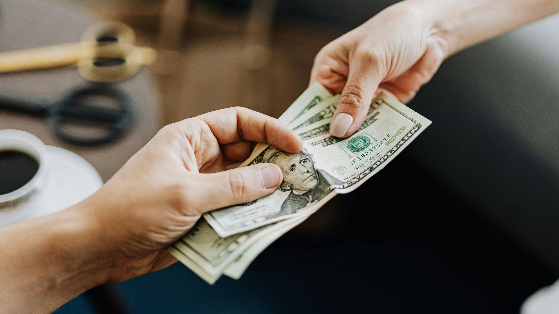 A close-up image of hands exchanging US dollar bills, symbolizing financial transaction or payment.