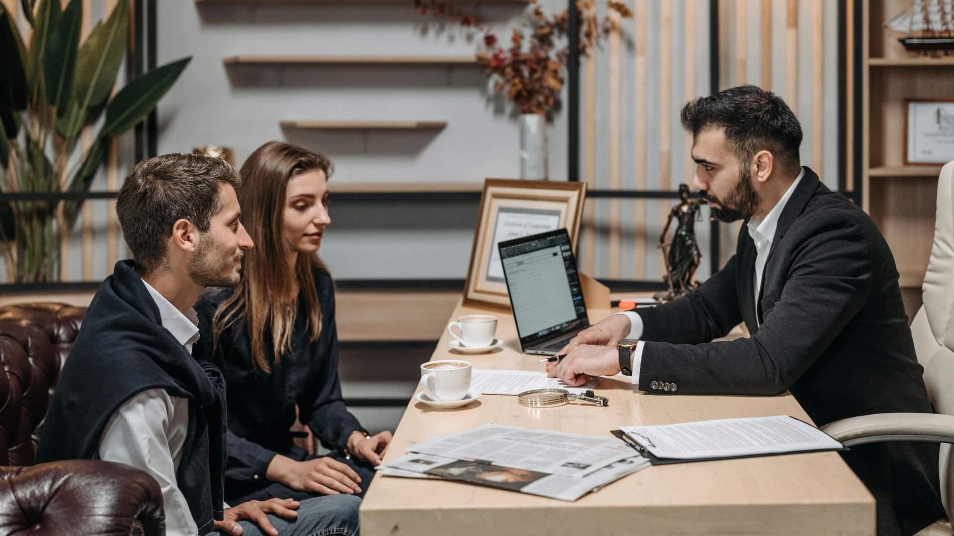 Three professionals engaged in a business discussion at an office desk with a laptop.