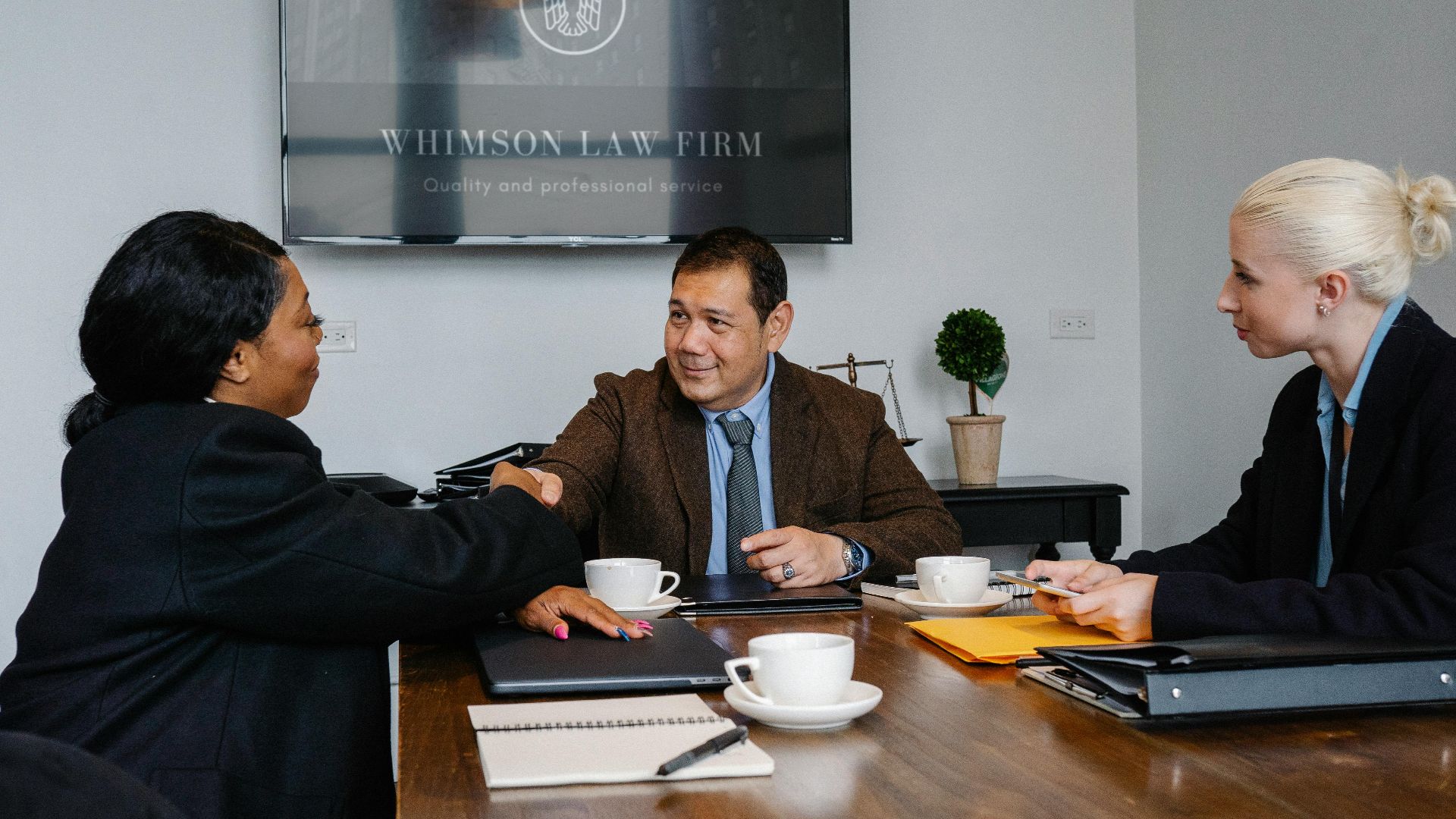 Group of multiracial coworkers in formal suits gathering at table with documents and coffee while shaking hands after verdict in court