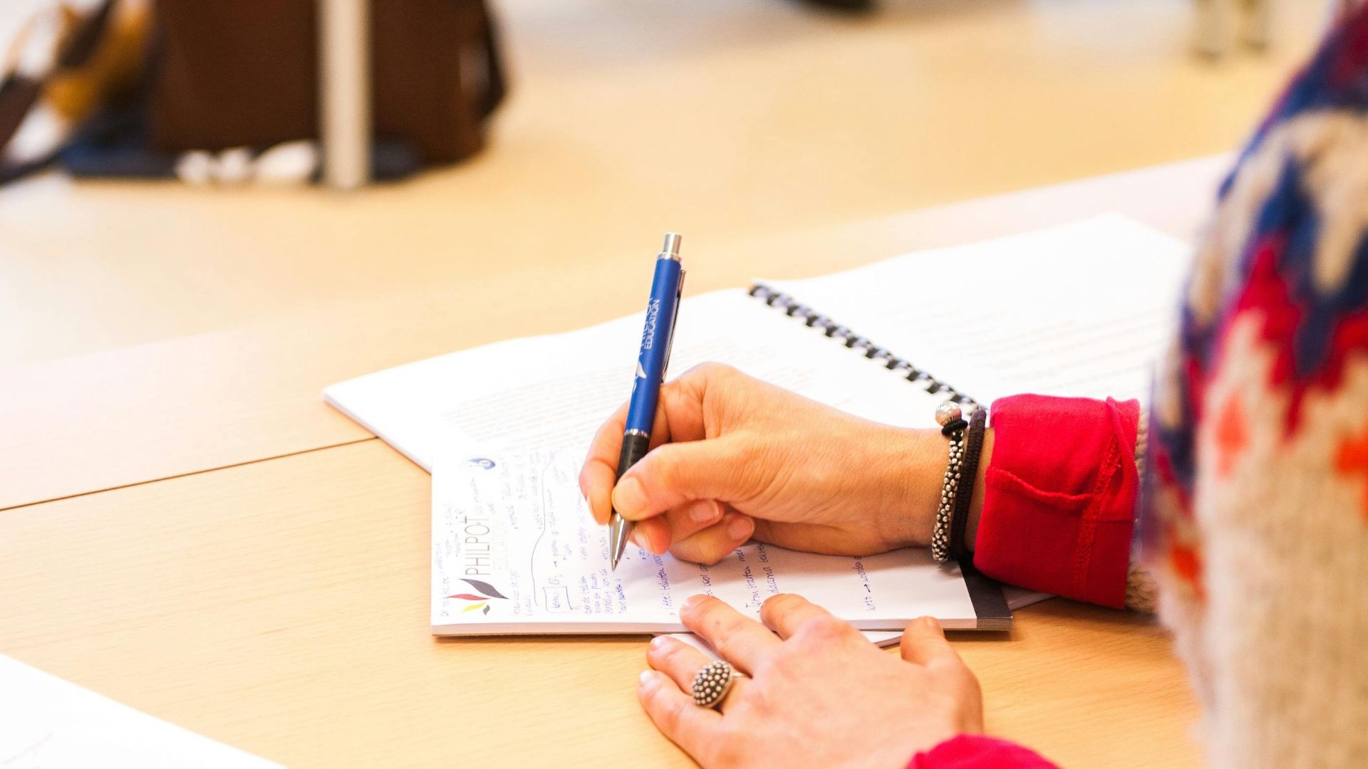 A woman writing notes in a notebook during a classroom lecture setting.