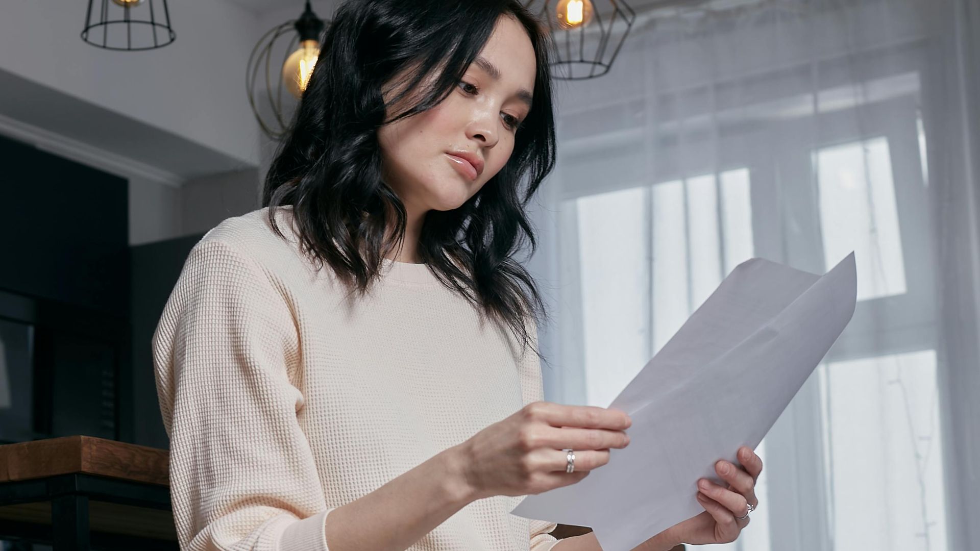 Casual woman reading documents in a stylish indoor setting with modern lighting.