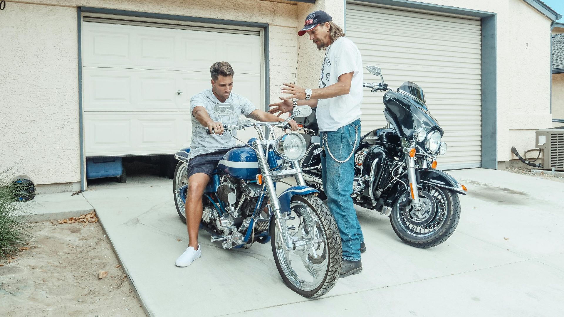 Two men enjoy quality time with motorcycles outside a garage, symbolizing parenthood and bonding.