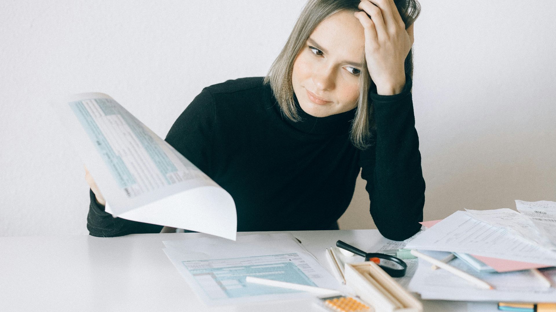 A woman showing stress while reviewing multiple paperwork and financial documents at a desk.