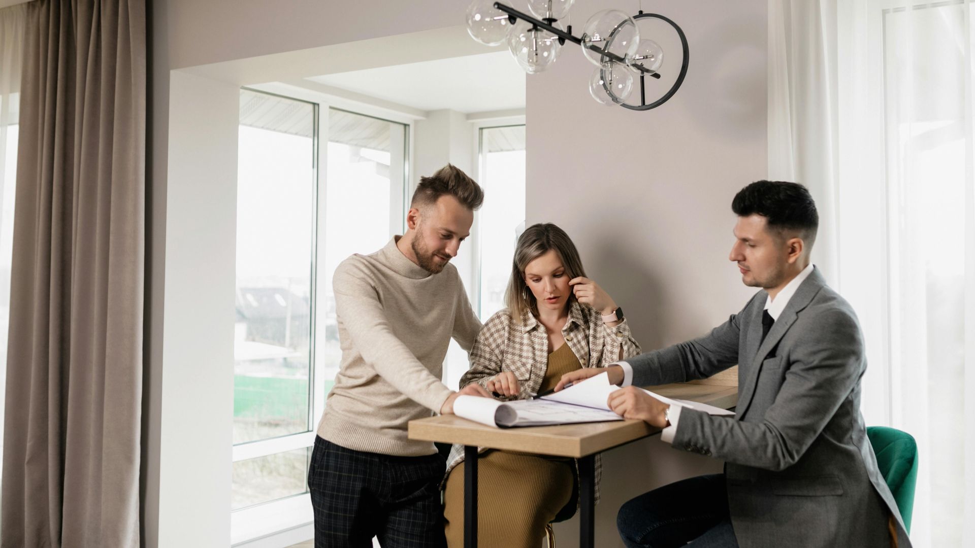 A couple consults with a real estate agent in a modern indoor setting, reviewing property documents.