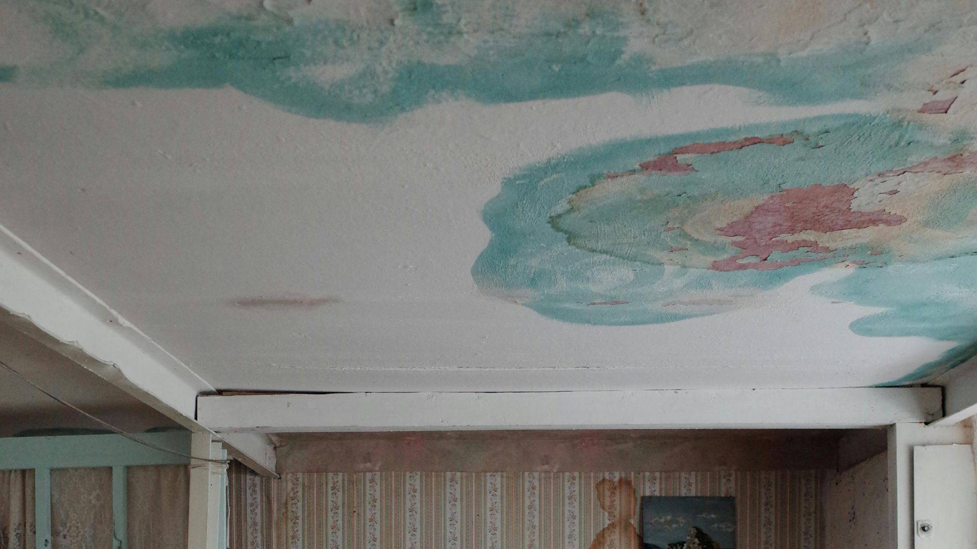 A small bedroom with a unique ceiling design, featuring water stains and an eclectic bed setup.