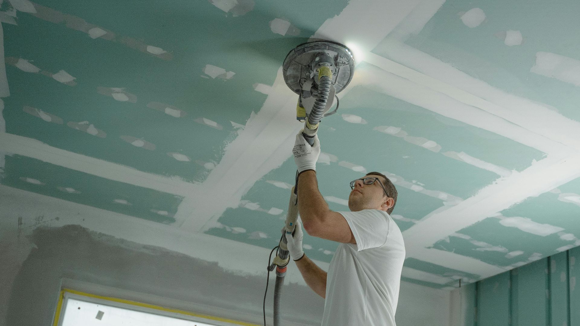 A professional worker sanding the ceiling during a home renovation project. Indoor construction setting.