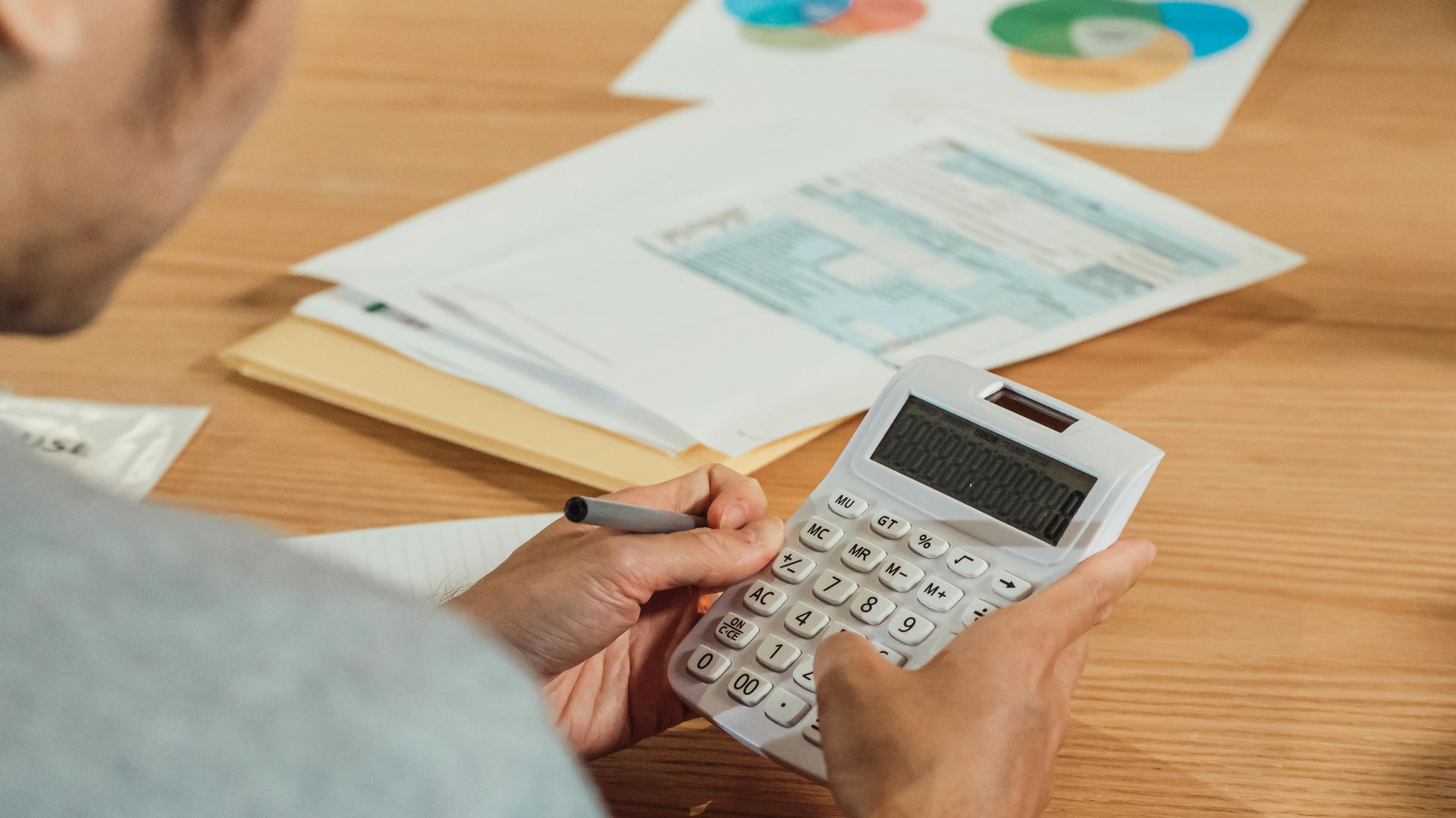 Person using a calculator at a desk with financial documents. Modern business concept.