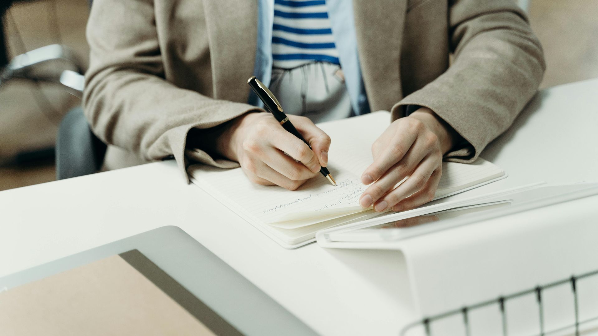 Close-up of an adult writing in a notebook at a modern office desk, capturing professional planning.