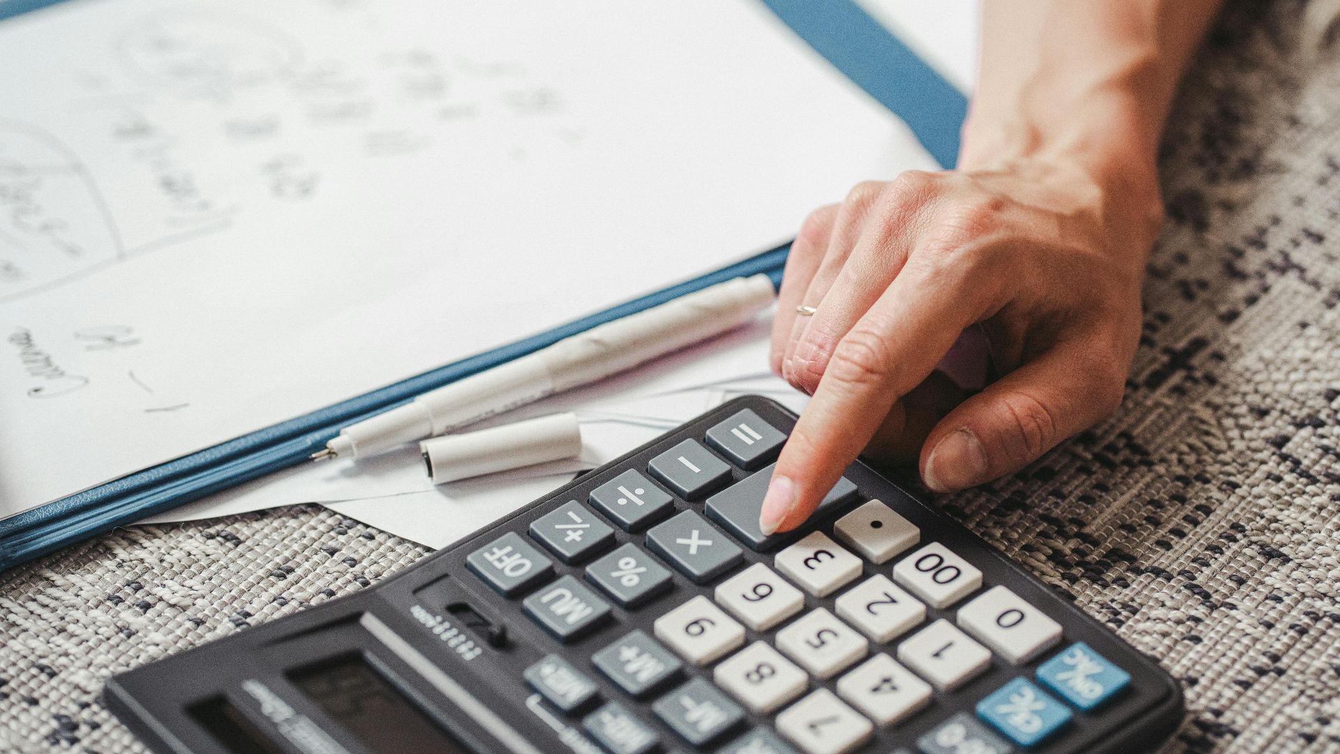 A hand using a calculator on top of documents, indicating financial calculation or analysis.