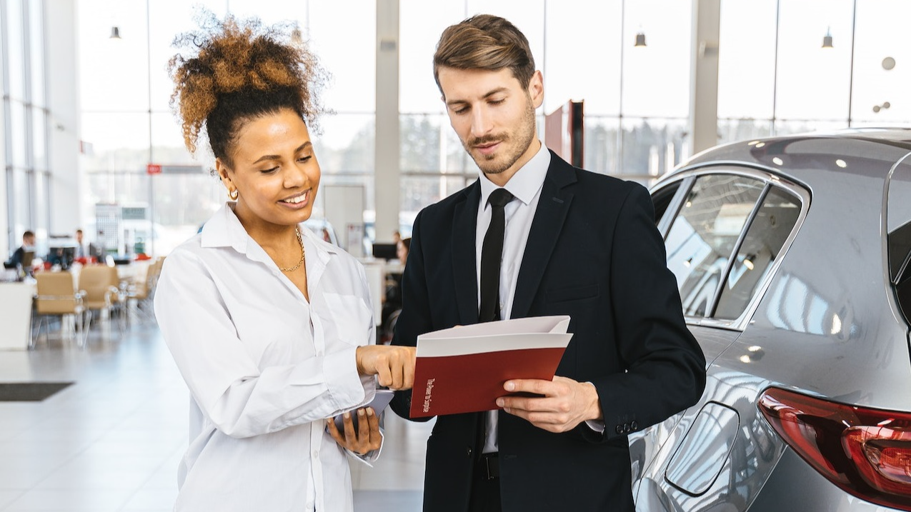 Man and woman are looking documents at car dealership.