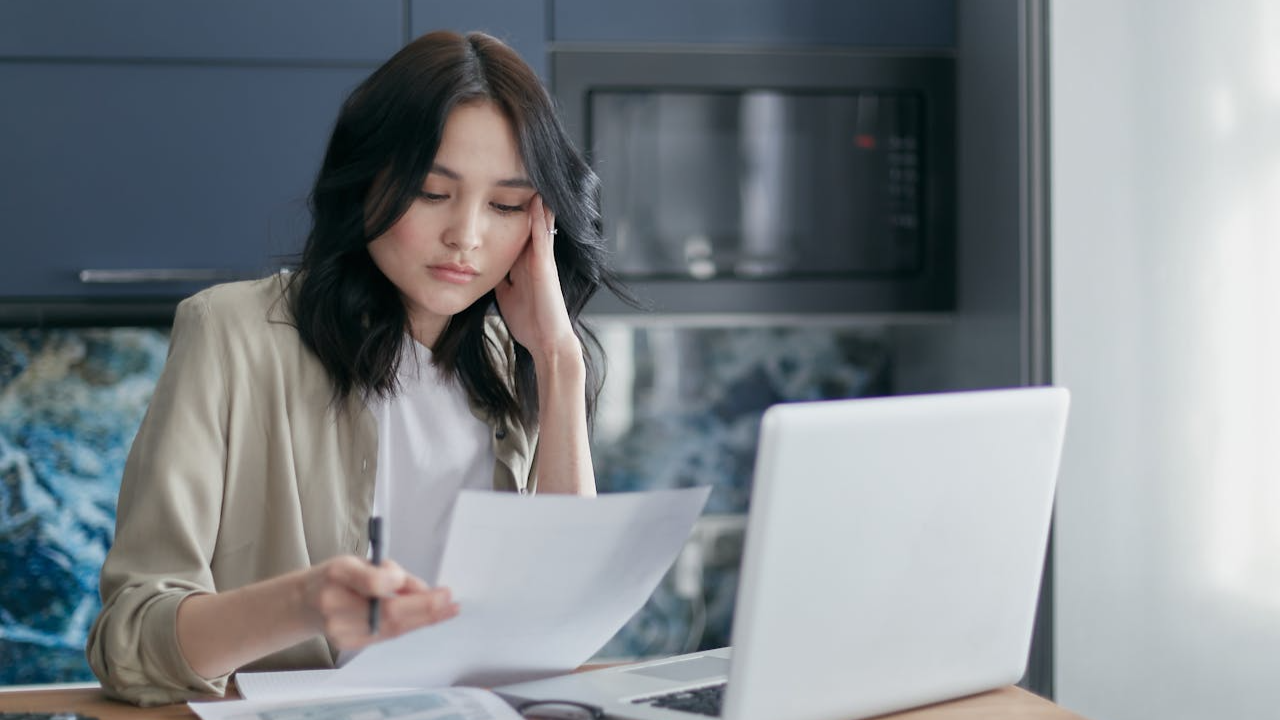 The image shows a woman with dark hair sitting at a table, seemingly engrossed in reviewing some documents