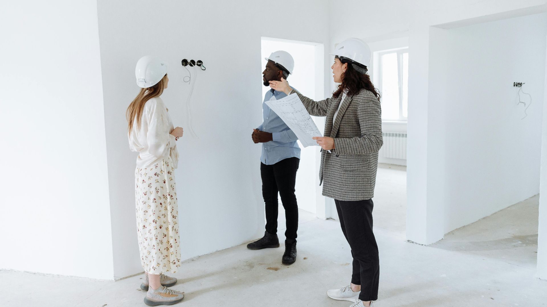 Three professionals discuss design plans inside a new house wearing hard hats.