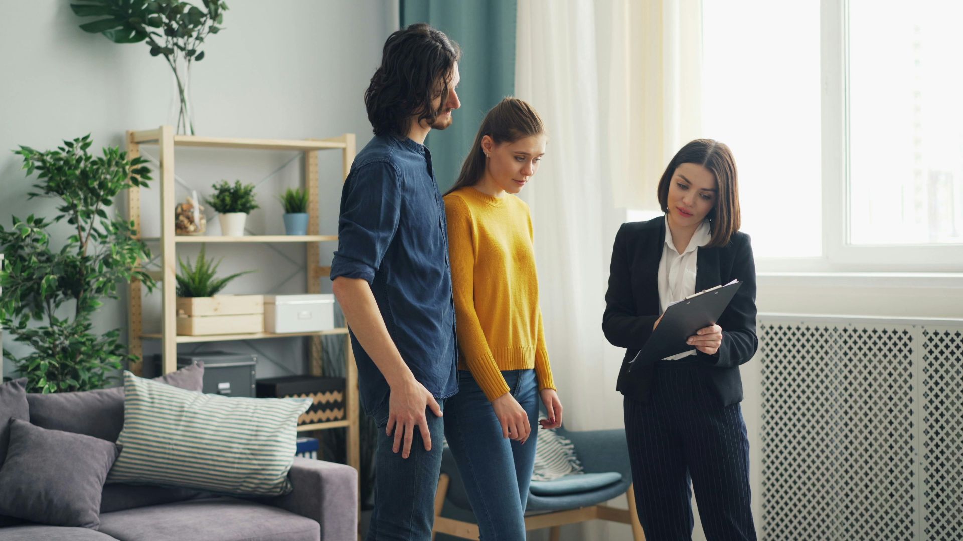 Real estate agent consulting a couple in a modern living room setting, surrounded by indoor plants.