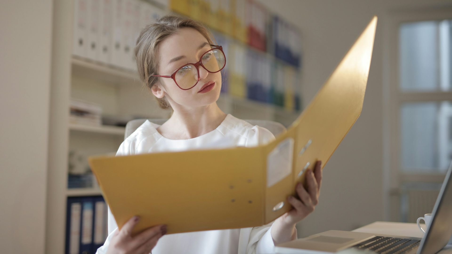 Caucasian woman intensely reading documents in an office setting.
