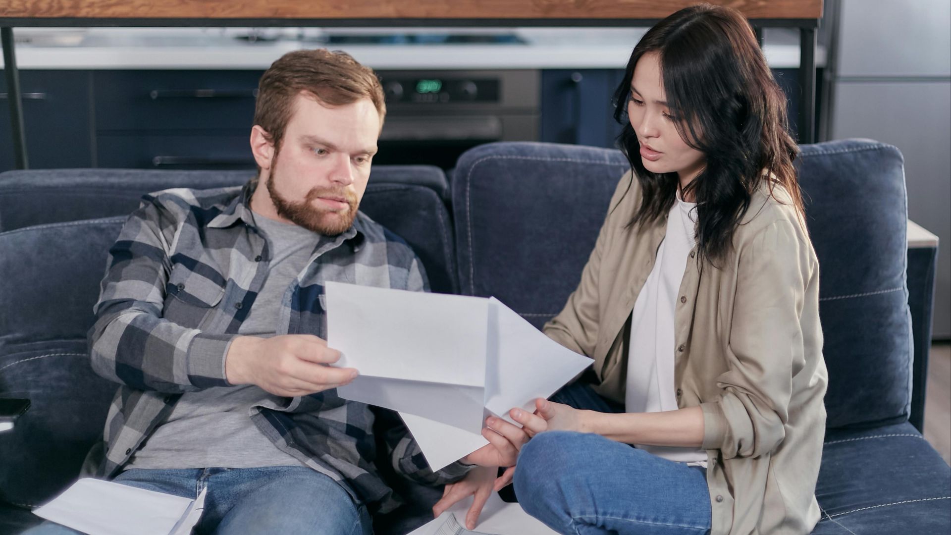 Asian woman and Caucasian man discussing taxes on couch.