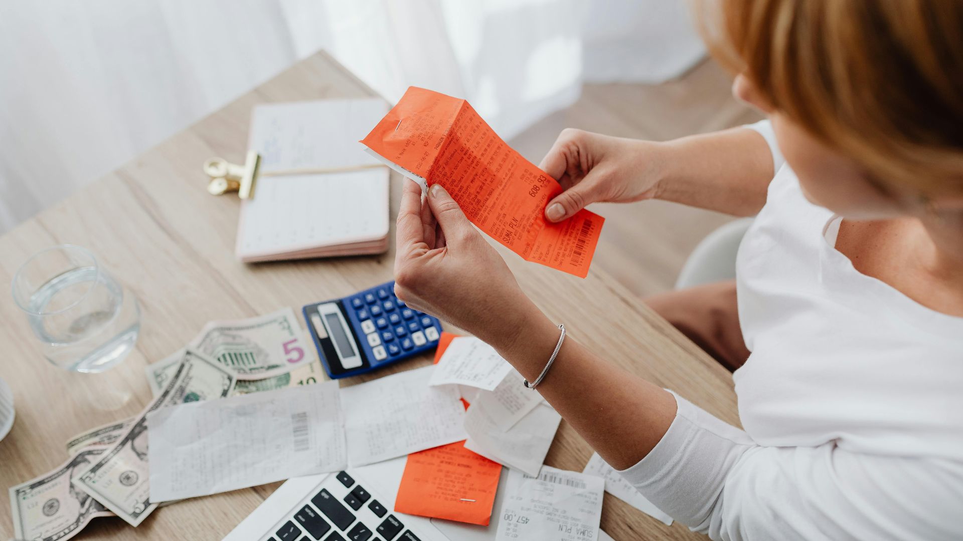 Woman using calculator and receipts at home office desk for finance management.